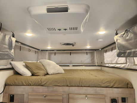 Inside an RV rental: a comfortable bedroom with a made bed, AC, ceiling fan, and soft-sided sleeping area.