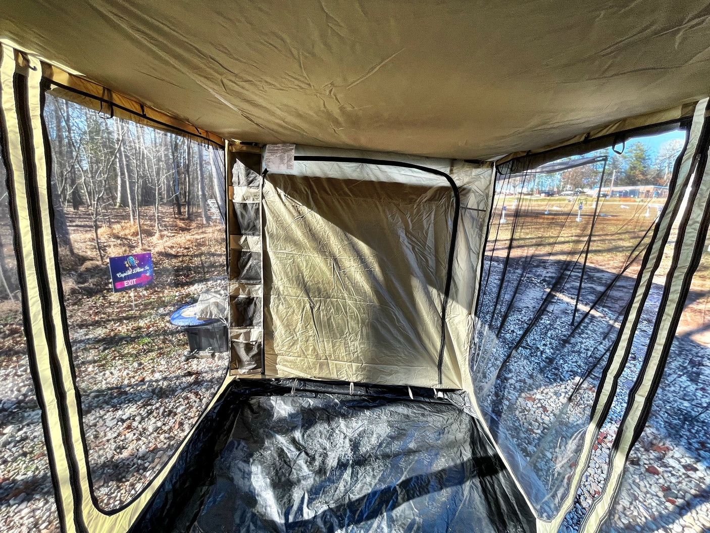 Inside an RV rental annex: clear walls offer outdoor views of a wooded area, with a privacy partition and tarp floor.
