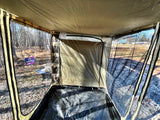 Inside an RV rental annex: clear walls offer outdoor views of a wooded area, with a privacy partition and tarp floor.