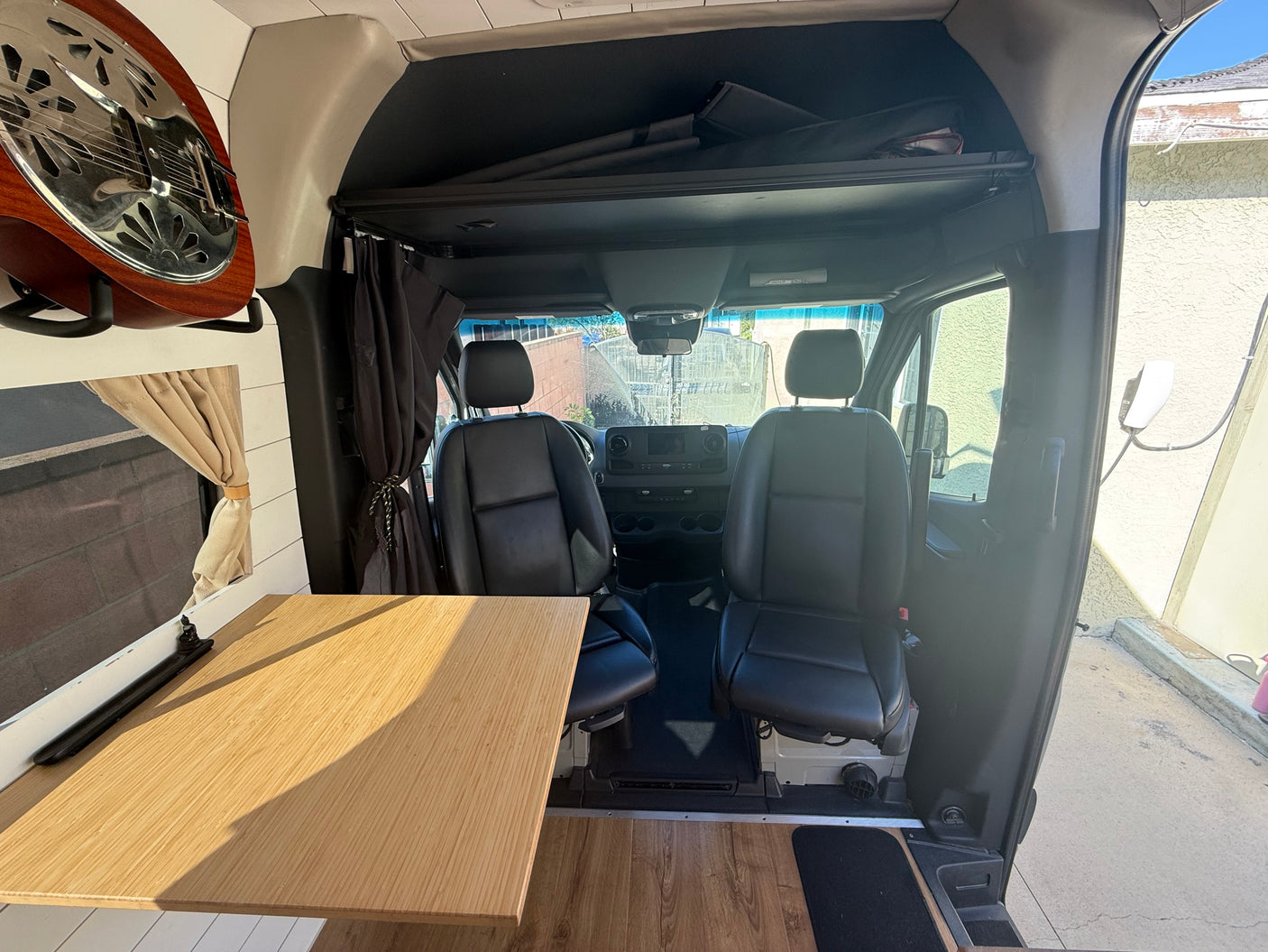 This RV rental camper van interior features a wooden table, driver's area, and a guitar, ideal for road trip adventures.