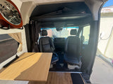 This RV rental camper van interior features a wooden table, driver's area, and a guitar, ideal for road trip adventures.