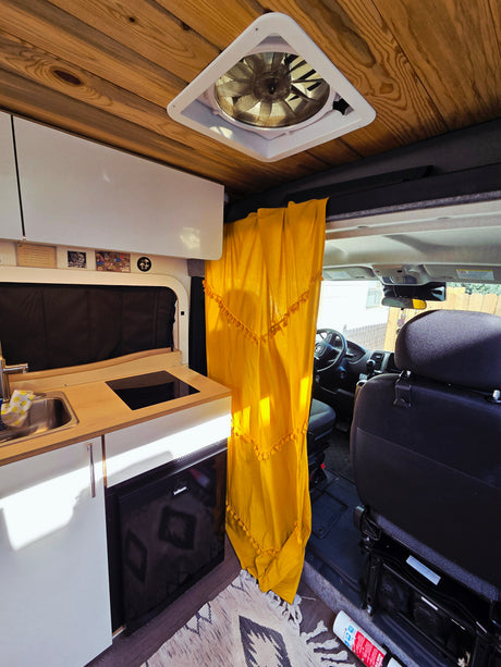 RV rental cozy van conversion with a wooden ceiling, kitchen sink, cooktop, fridge, and a vibrant yellow privacy curtain.