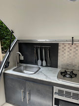 RV rental compact kitchen: stainless steel sink, gas stove, microwave, and utensil rack. Perfect for adventurers.