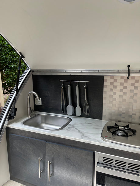 RV rental compact kitchen: stainless steel sink, gas stove, microwave, and utensil rack. Perfect for adventurers.