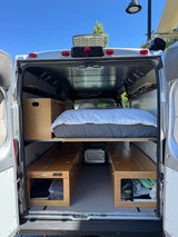 Inside a camper van RV rental: compact bed and practical under-bed storage boxes for road trip living.