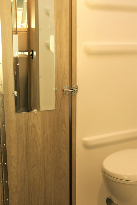 RV rental: Compact bathroom with toilet, built-in shelves, and a door featuring a mirror, optimizing space.