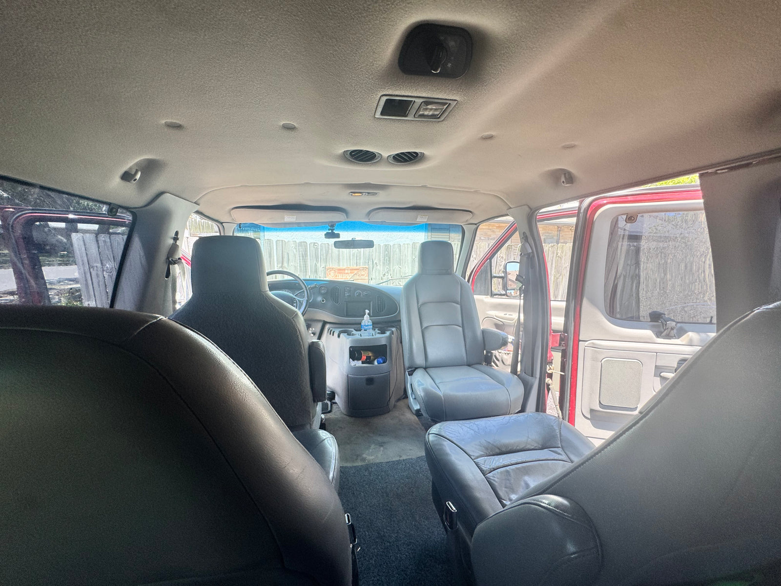 Interior view of an **rv rental** van with gray seats, visible dashboard, overhead controls, and open side doors letting in natural light.