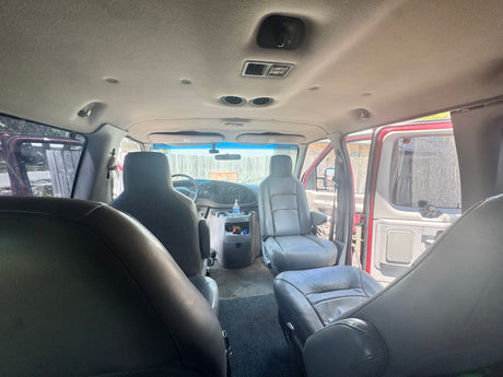 Interior view of an **rv rental** van with gray seats, visible dashboard, overhead controls, and open side doors letting in natural light.