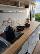 Compact and modern RV kitchen with wooden countertop, induction cooktop, kettle, and storage. Great for an RV rental getaway.