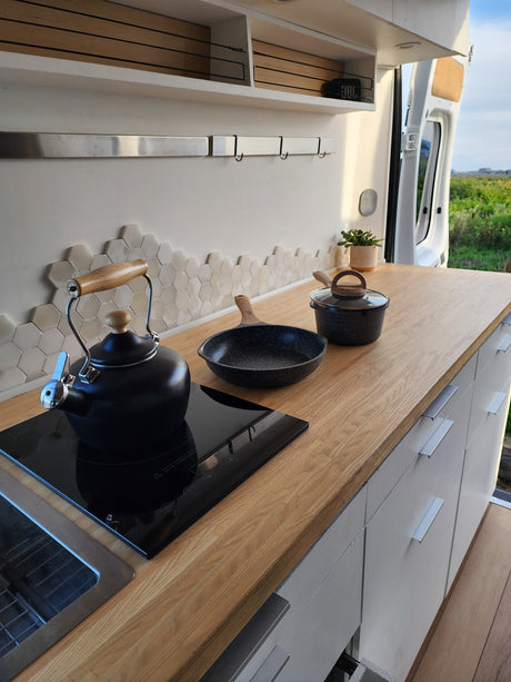 Compact and modern RV kitchen with wooden countertop, induction cooktop, kettle, and storage. Great for an RV rental getaway.
