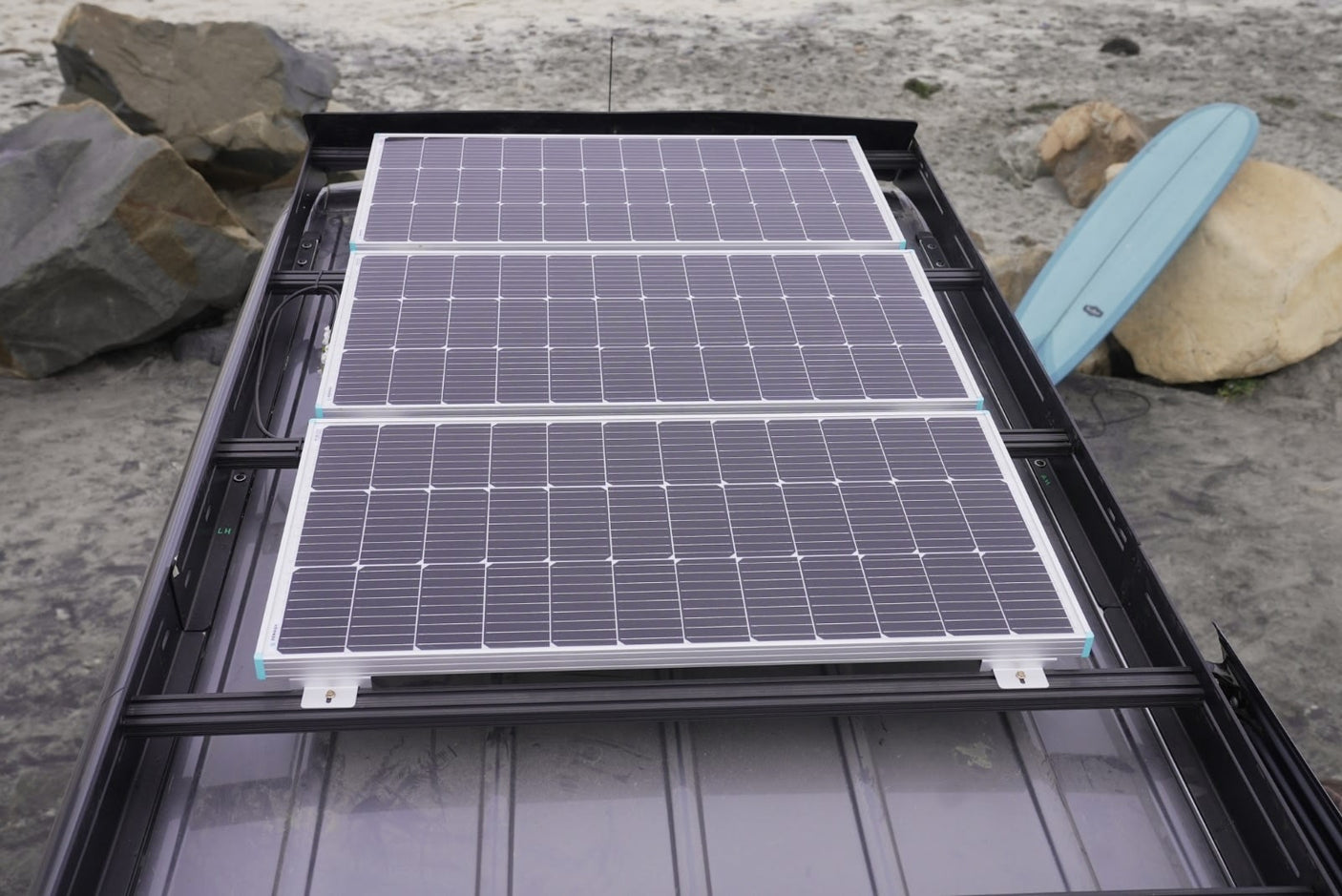 RV rental with three rooftop solar panels for off-grid beach adventures. Surfboard visible.