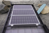 RV rental with three rooftop solar panels for off-grid beach adventures. Surfboard visible.