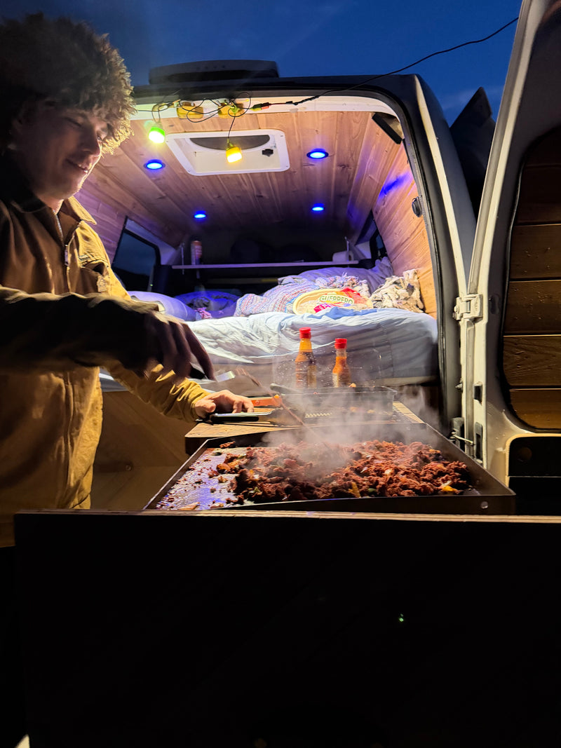 Enjoying a delicious meal cooked on a griddle outside an RV rental at night. Cozy van life with string lights & blue accents. — photo 6