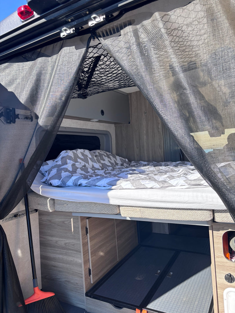 RV rental interior featuring a comfortable bed, overhead storage net, under-bed storage, and a protective bug screen. — photo 6