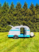 This charming white & blue Retro Jr. teardrop camper, ideal for RV rental, sits on a vibrant green lawn under blue skies.