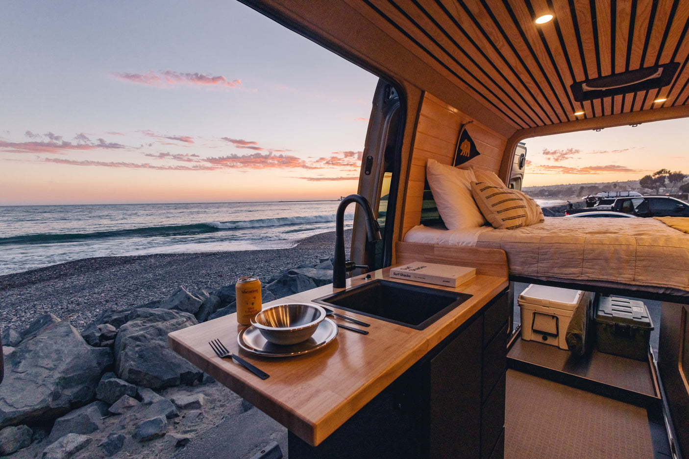 Stunning sunset ocean view from an RV rental camper van, featuring a cozy interior with a kitchen and bed.