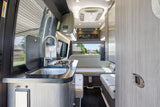 Inside this RV rental: a compact kitchen with sink/stovetop, comfortable lounge seating, and bright interior.