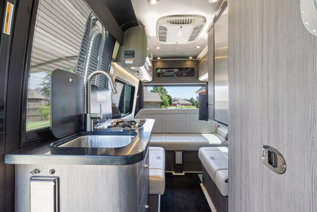 Inside this RV rental: a compact kitchen with sink/stovetop, comfortable lounge seating, and bright interior.