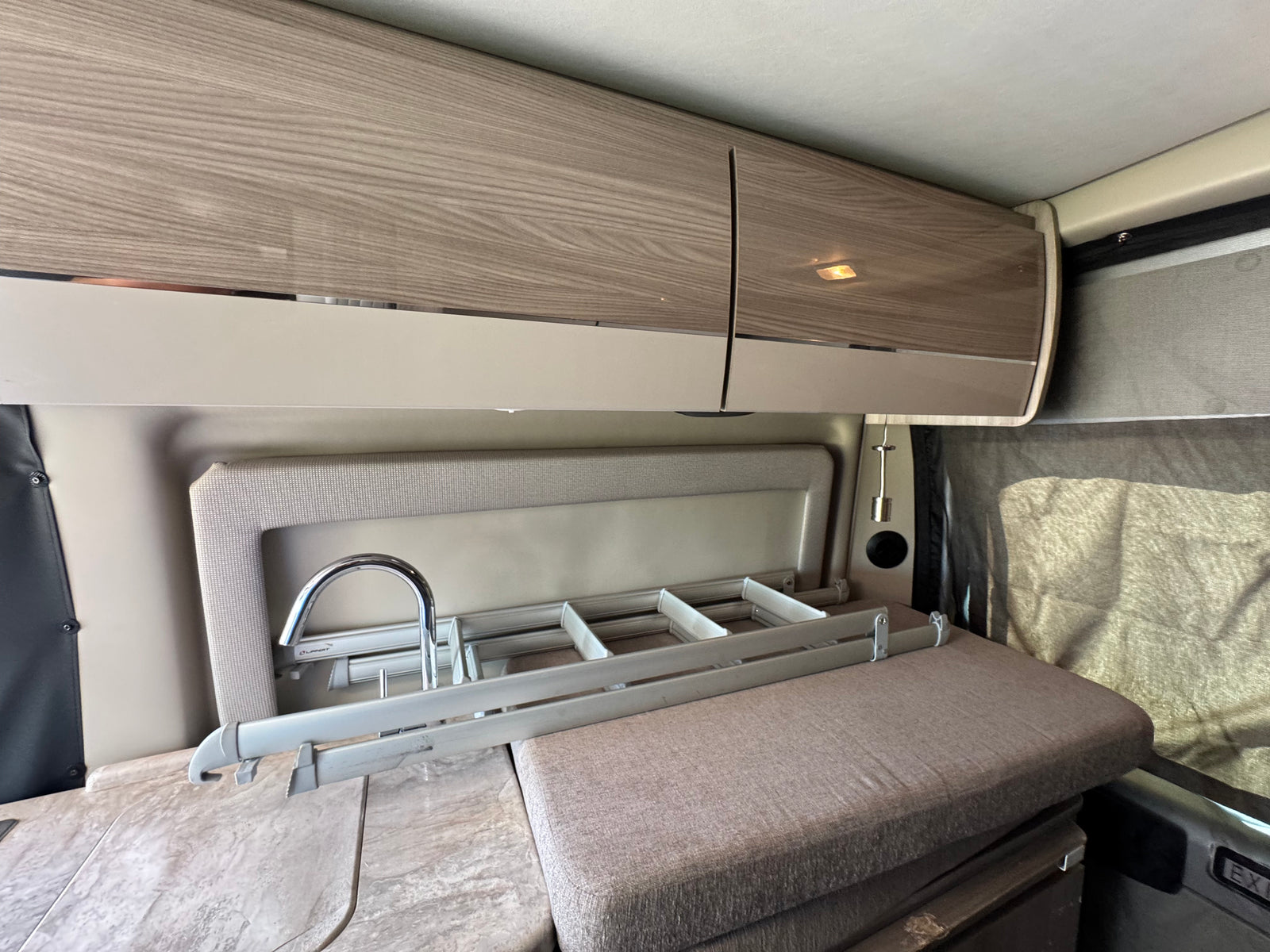 Explore this RV rental's compact kitchen with wood-look cabinets, sink, collapsible drying rack, and comfortable seating.