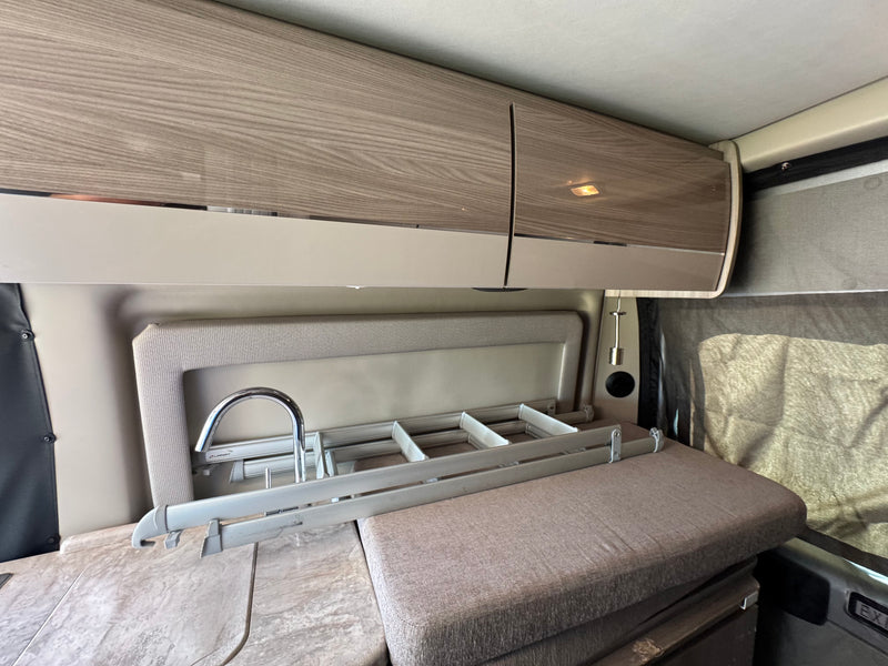 Explore this RV rental's compact kitchen with wood-look cabinets, sink, collapsible drying rack, and comfortable seating. — photo 11
