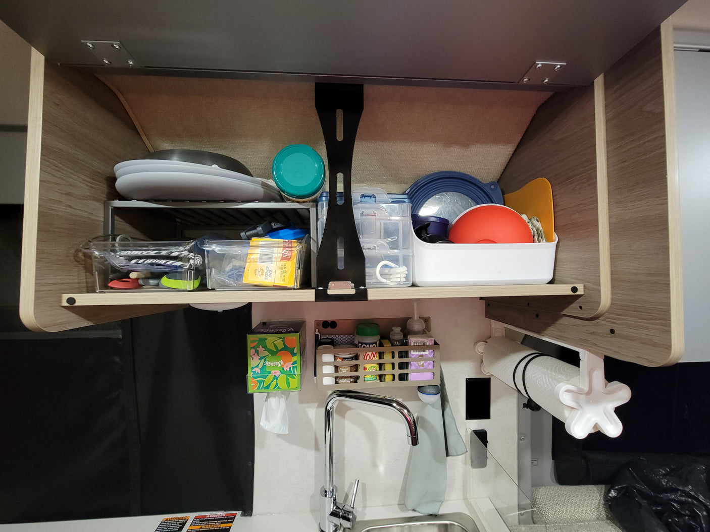 Organized RV rental kitchen cabinet with dishes, spices, and sink, showing practical storage solutions for travel.