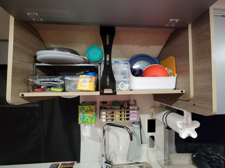 Organized RV rental kitchen cabinet with dishes, spices, and sink, showing practical storage solutions for travel.