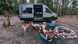Family enjoying their RV rental: Kids relaxing by a campfire with their dog in a serene forest campsite.