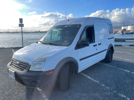 White Ford van for ebike rentals, similar to a small rv rental vehicle, parked by a sunny harbor.