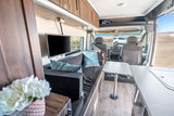 Spacious RV rental interior: A modern campervan lounge with TV, kitchen counter, and cockpit area, ready for travel.