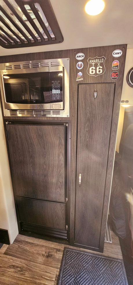 Compact RV rental kitchenette featuring a microwave, refrigerator, and ample storage, perfect for road trip adventures.