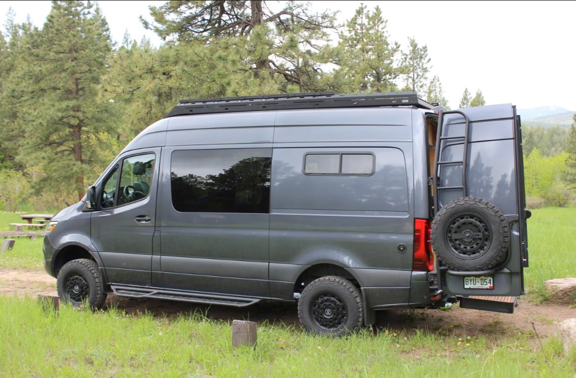 Rugged grey camper van, parked in nature with roof rack & rear spare tire. Ideal rv rental for scenic escapes. — photo 10
