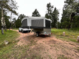 An RV rental pop-up camper and white SUV parked on a dirt road, set up for camping in a scenic forest.