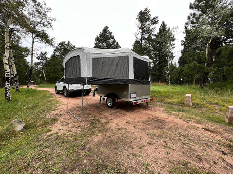 An RV rental pop-up camper and white SUV parked on a dirt road, set up for camping in a scenic forest.