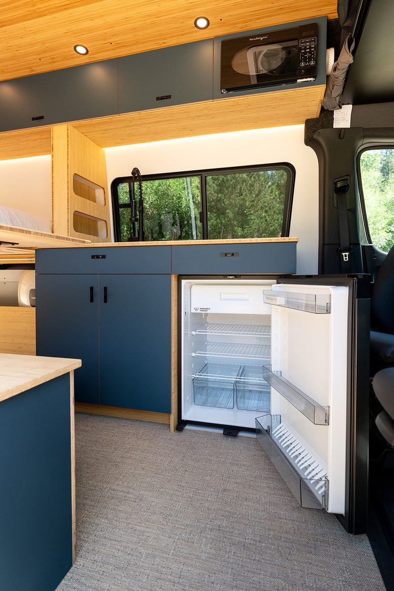 Modern RV rental kitchen with open fridge, microwave, bamboo walls, and blue cabinetry. — photo 5