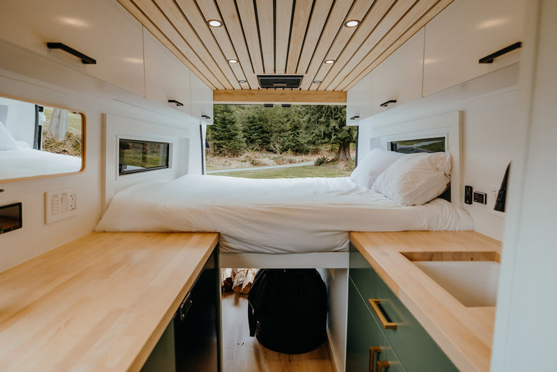 Modern **rv rental** camper van interior: elevated bed, wood ceiling/counters, forest view. Ideal for road trip comfort. — photo 5