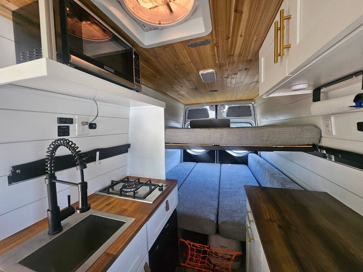 Cozy camper van rv rental interior: kitchen with microwave, sink, stove, and a versatile bunk bed sleeping area.