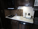 RV rental: a functional kitchen with stove, sink, microwave, and fridge. Compact design with tiled backsplash.