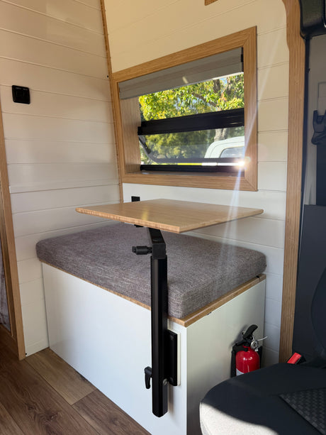 Cozy RV rental interior with a versatile table, comfortable bench seating, window view, and a readily accessible fire extinguisher.