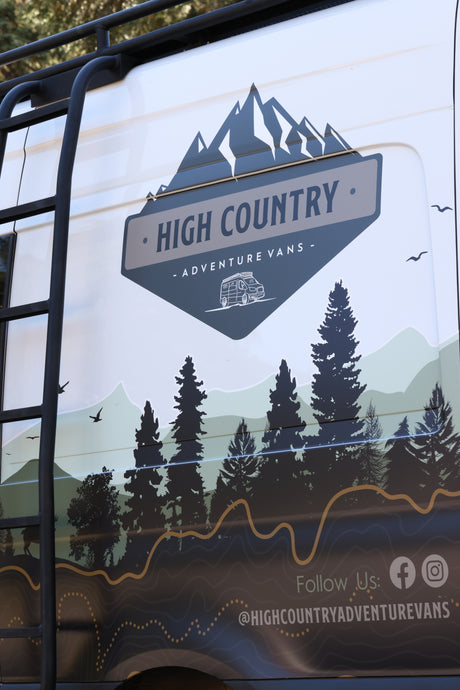 Side of a High Country Adventure Vans RV rental, featuring a custom graphic with mountains, trees, and social info.
