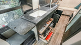 Compact RV rental kitchen with a black countertop, sink, cooktop, and organized pull-out drawers for utensils.