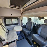 Spacious RV rental interior showing swiveling driver seats, passenger bench, & small table. Perfect for your next road trip adventure.