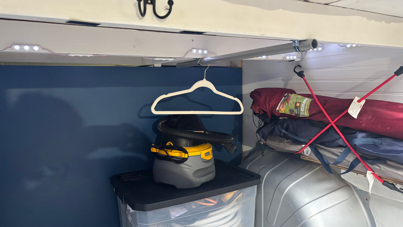 Inside an RV rental: LED lights illuminate storage. A shop vac sits on a bin, a hanger is above, and camping gear is stacked.