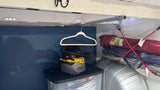 Inside an RV rental: LED lights illuminate storage. A shop vac sits on a bin, a hanger is above, and camping gear is stacked.