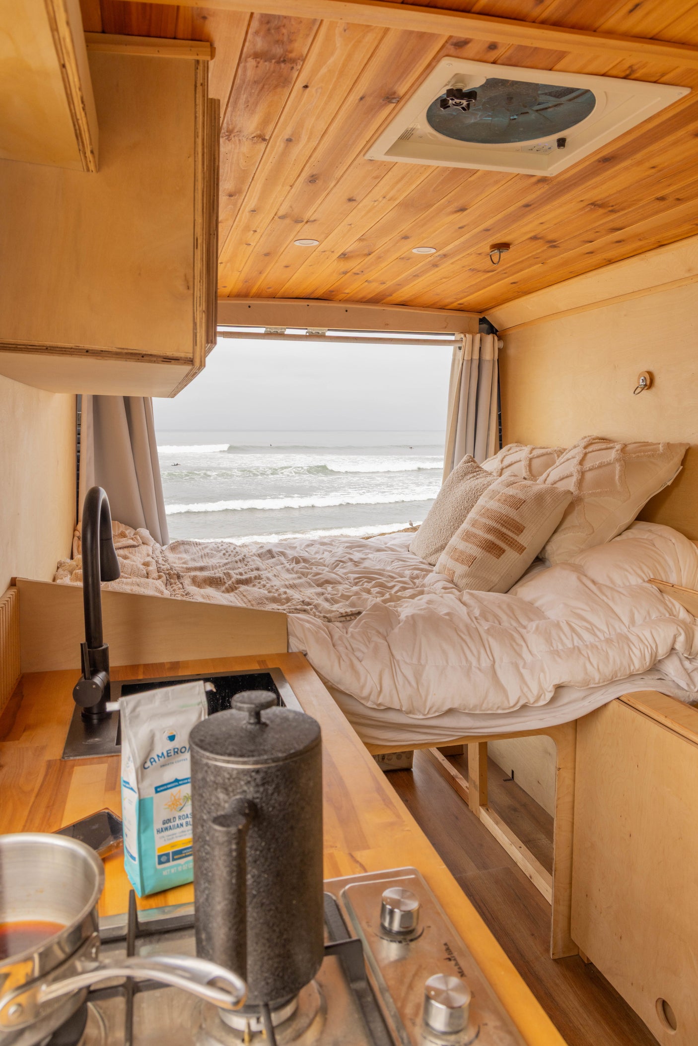 Experience van life in this rv rental, featuring a cozy bed with ocean views, a compact kitchenette, and wooden interiors.