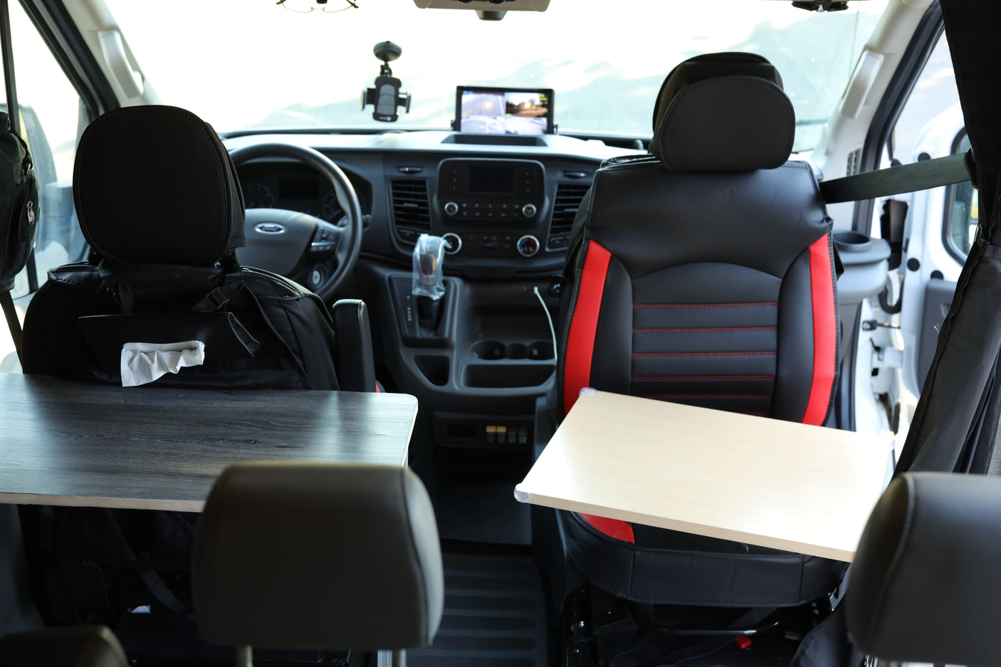 This RV rental interior features front seats, each with a small table, facing the organized dashboard, ideal for travel.