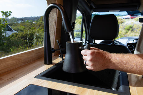 Filling a kettle in an RV rental kitchen with a scenic view of nature from the window.