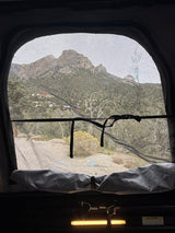 From an RV rental pop-top, a clear mountain view through a mesh screen, with distant homes and trees on the hillside.