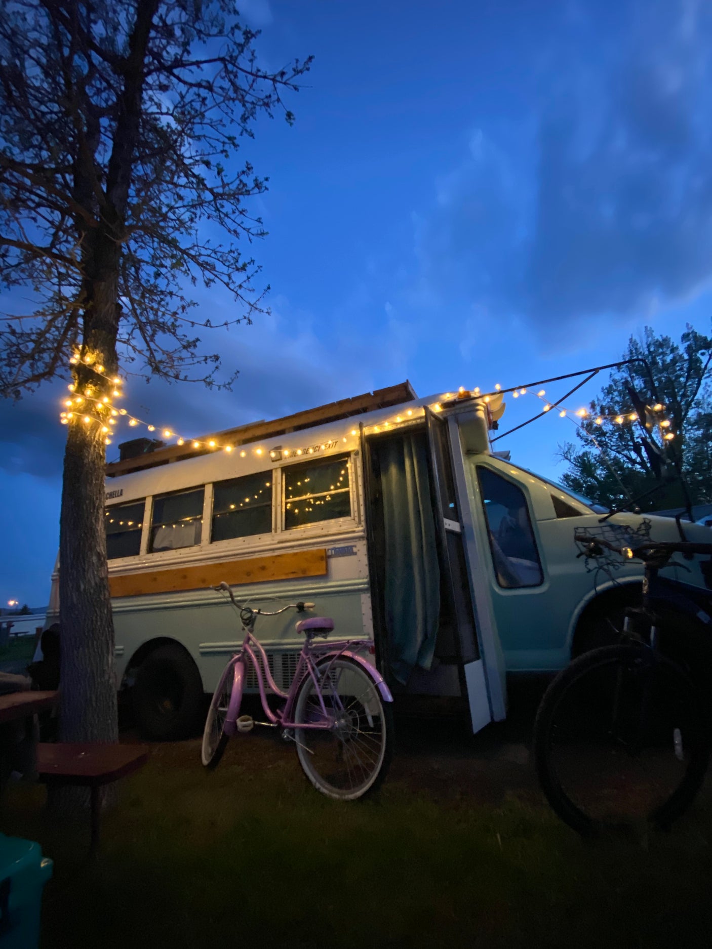 Cozy RV rental: converted bus at dusk with string lights and a pink bicycle.