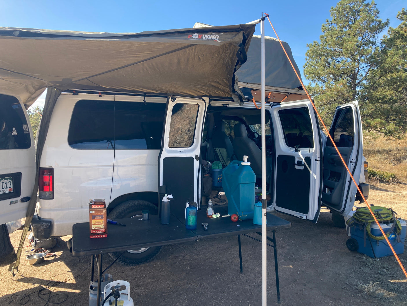 White converted van with awning & rooftop tent set up for camping. An ideal RV rental for outdoor adventures & van life.