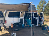 White converted van with awning & rooftop tent set up for camping. An ideal RV rental for outdoor adventures & van life.